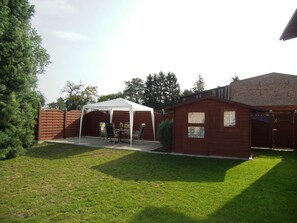Ein Garten mit einem weißen Zelt, einem Holler Schuppen und einem Backsteinhaus.