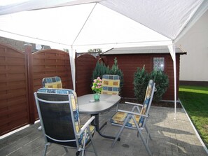 Eine Terrasse im Freien mit einem runden Tisch, vier Stühlen, einem Blumentopf und einem Holzzaun.