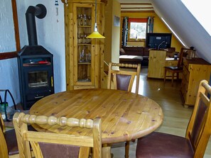 A cozy, wood-furnished room with a central table, chairs, a built-in wood stove, and a television.