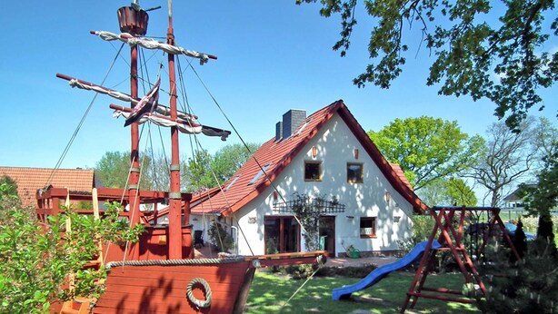 A wooden ship model, a white house with a red roof, and a playground with a slide.