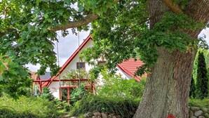 A house with a red roof, surrounded by greenery and a large tree.