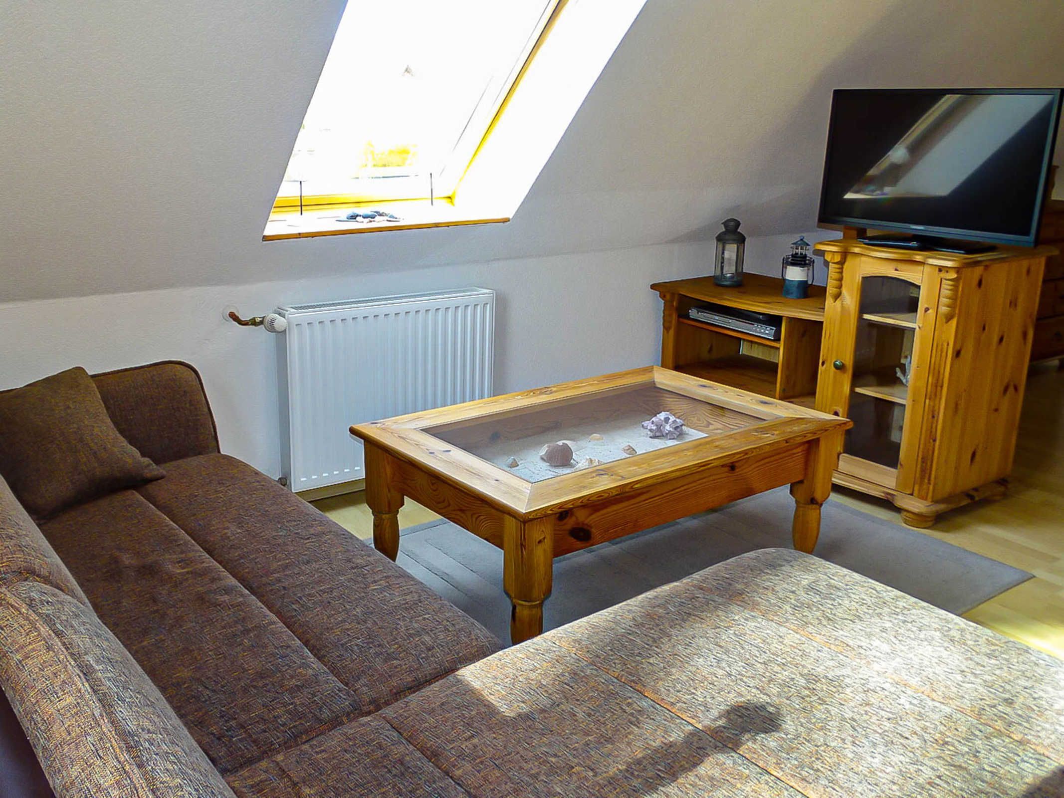 Une pièce de style « loft » avec un plafond en pente, un canapé, une table basse, un téléviseur posé sur un meuble en bois et un radiateur.