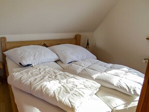 Ein Einzelbett mit Holz-Kopfteil, weißer Bettwäsche und einer an der Wand befestigten Leuchte.
