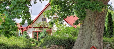 A house with a red roof, surrounded by greenery and a large tree.