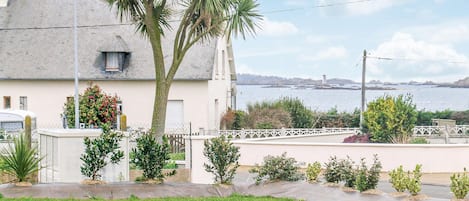 Una casa costera con fachada blanca, un balcón y vista al mar.