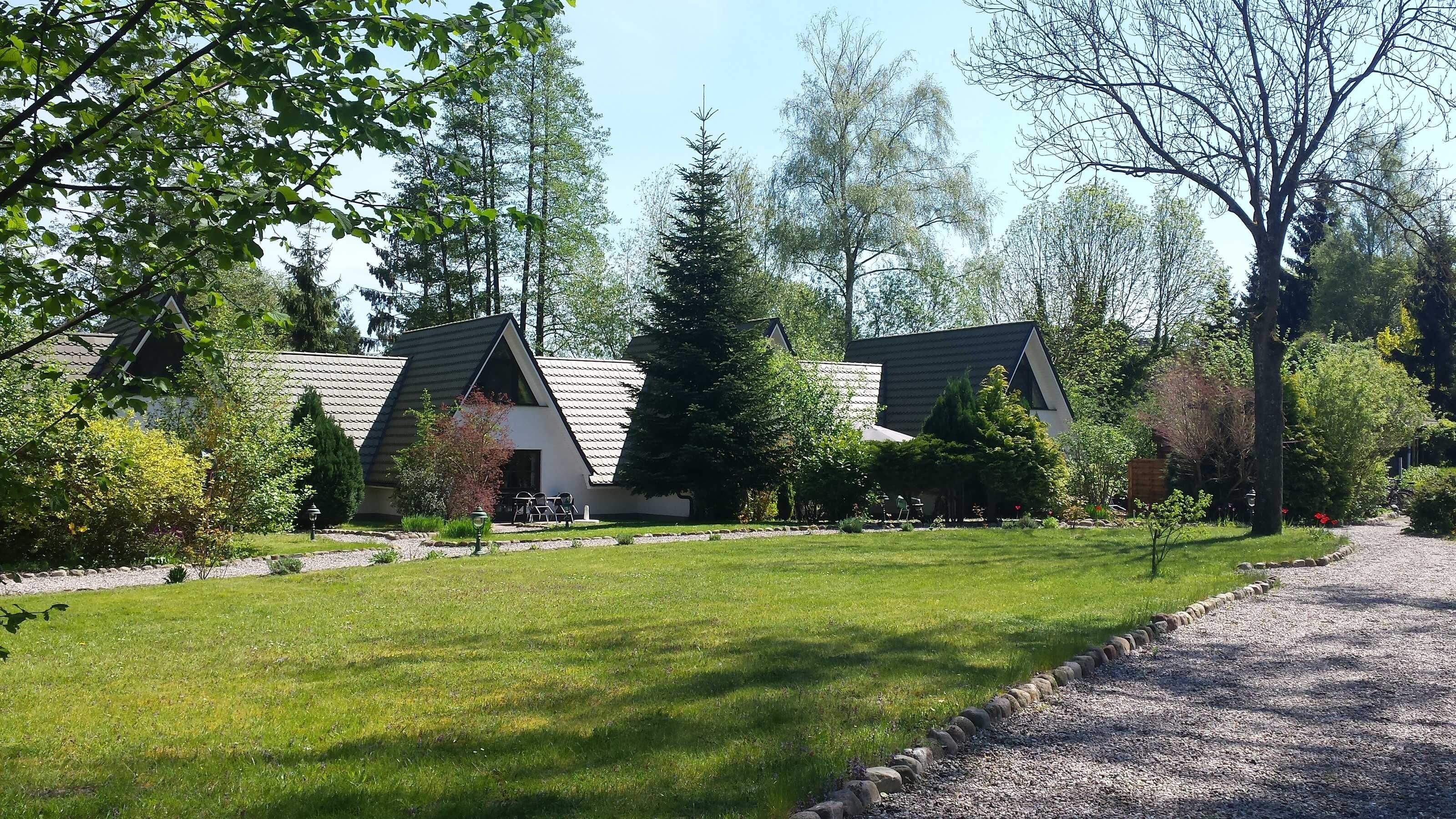 A row of modern, single-story cabins with sloped roofs, surrounded by a well-maintained lawn and trees.