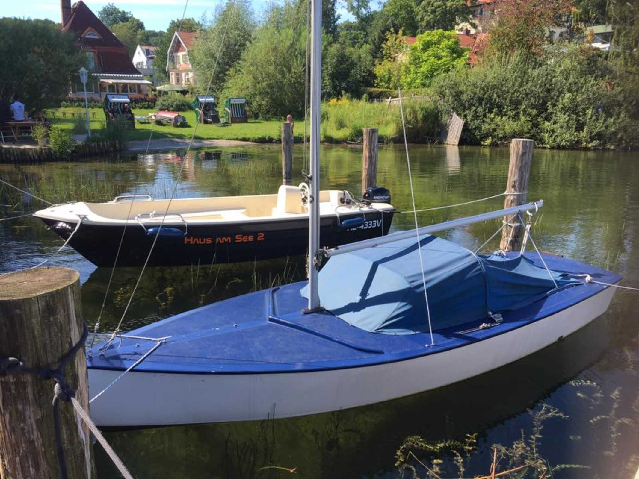 Two boats docked at a pier with a house and greenery in the background.