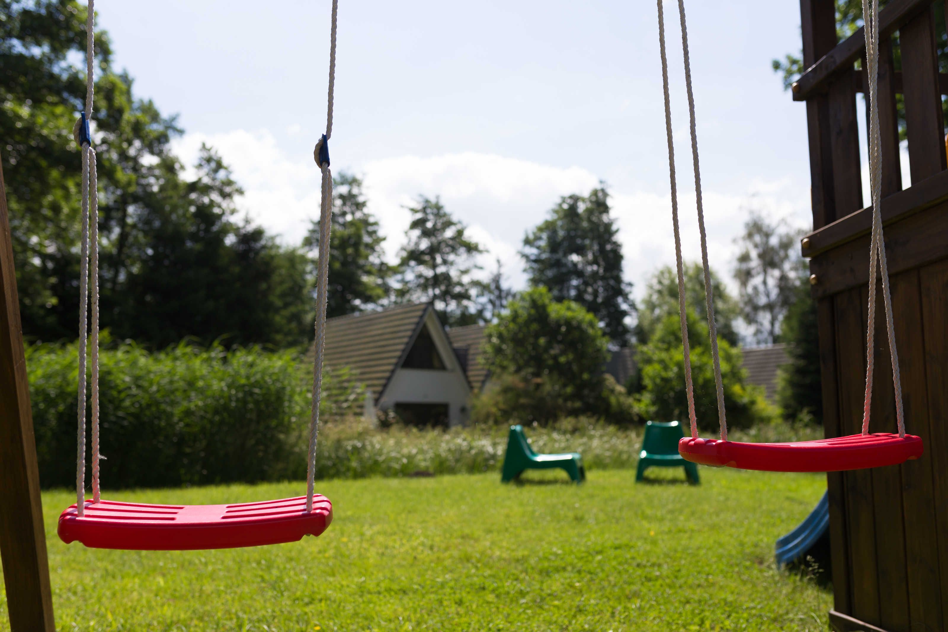 A swing set with two swings, a green chair, and a slide in a backyard.