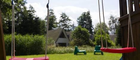 Un portique avec deux balançoires, une chaise verte et un toboggan dans un jardin.