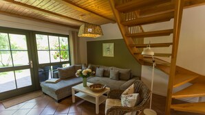 A cozy living room with a sofa, a coffee table, a wicker chair, a floor lamp, and a wooden staircase.