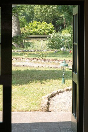 A garden view through a doorway with a stone pathway, a green lamp post, and a variety of plants and trees.