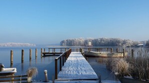 Une jetée enneigée s’avance sur un lac paisible, avec une île boisée en arrière-plan.