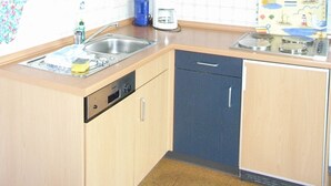 Une cuisine compacte dotée de meubles en bois, d’un lave-vaisselle, d’une machine à café et d’une cuisinière.