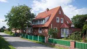 Une maison en briques rouges, avec un toit en pente, une clôture verte et une allée pavée.