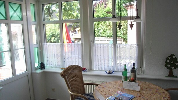 Un coin repas avec une table ronde, des chaises en osier et une vue sur l’extérieur grâce à de grandes fenêtres.