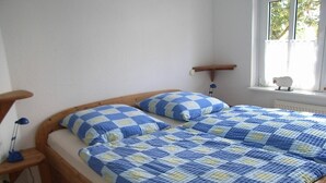 Un lit en bois avec une couvre-lit à carreaux bleus et jaunes et des coussins assortis, une table de chevet avec une lampe, et une fenêtre avec un rideau.