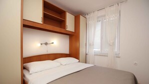 Quarto com cama, cabeceira de madeira, guarda-roupa embutido e janela com cortinas.