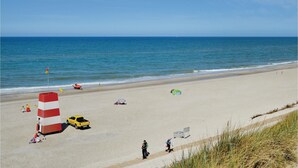 Una platja amb una torre de socorristes, un vehicle groc i gent passejant al costat de la riba.