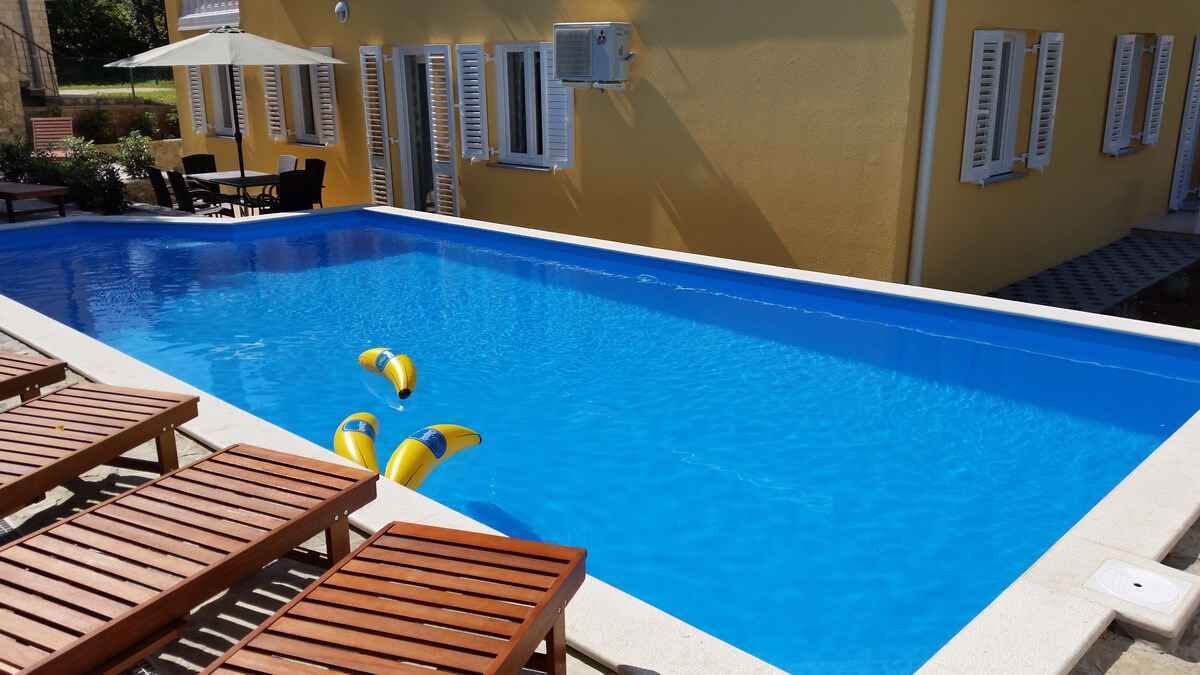 A swimming pool with wooden lounge chairs and inflatable toys.