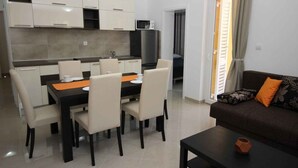 A modern kitchen with white cabinets, a black countertop, and a dining area with a black table and beige chairs. - Holiday apartment with shared pool and barbecue (Baška)