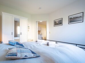 Une chambre à coucher comprenant un lit, une armoire et une porte donnant sur la cuisine.