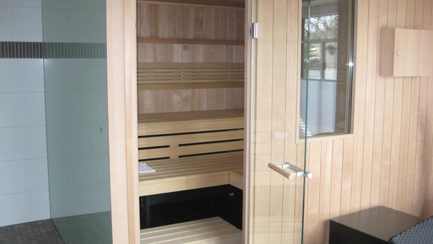 A sauna room with wooden benches, a glass door, and a small table. - 3-room 104 Jordland Balk Spülm. (BC 5) - BUE - Apartment house Westwind (Büsum)