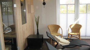 A room with a wooden wall, a black table, two wicker chairs, and a large window. - 3-room 104 Jordland Balk Spülm. (BC 5) - BUE - Apartment house Westwind (Büsum)
