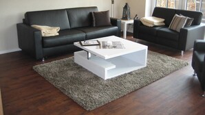 A modern living room with a black leather sofa, a white coffee table, and a grey rug. - 3-room 104 Jordland Balk Spülm. (BC 5) - BUE - Apartment house Westwind (Büsum)