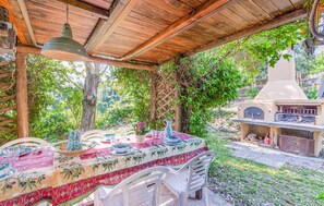 Ein Essbereich im Freien mit überdachter Terrasse, einem Tisch gedeckt mit Geschirr und Gläsern sowie einem Grill im Hintergrund.