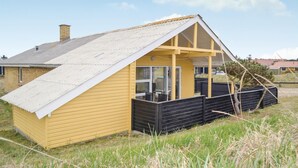 Un bâtiment jaune avec un toit en pente et une terrasse noire.