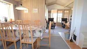 Un coin repas accueillant avec des chaises et une table en bois, une cuisine équipée d’une cuisinière, et un espace de vie avec un canapé et un téléviseur.