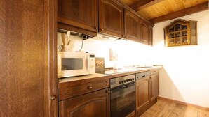 A kitchen with wooden cabinets, a microwave, a stove, and a window with a view of the outside. - Apartment 3 - Fewos "Storchenhof" near the lake (Meesiger)