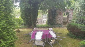 A garden patio with a table and chairs, surrounded by greenery and a stone wall. - Apartment 3 - Fewos "Storchenhof" near the lake (Meesiger)