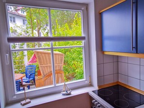 Een keuken met een groot raam, een eethoek met buitenmeubilair en uitzicht op groen en gebouwen.