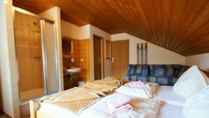 Een slaapkamer met een houten plafond, een bed met witte lakens, een douchegedeelte en een badkamer met een wastafel.