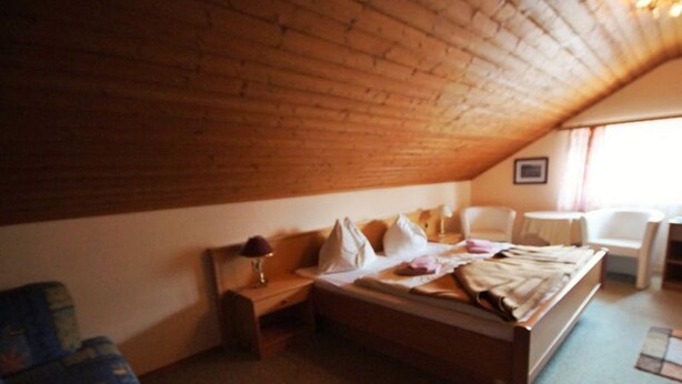 Een slaapkamer met een houten plafond, een bed, een stoel en een klein tafeltje.