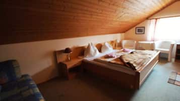 Quarto com teto de madeira, uma cama, uma cadeira e uma mesinha.