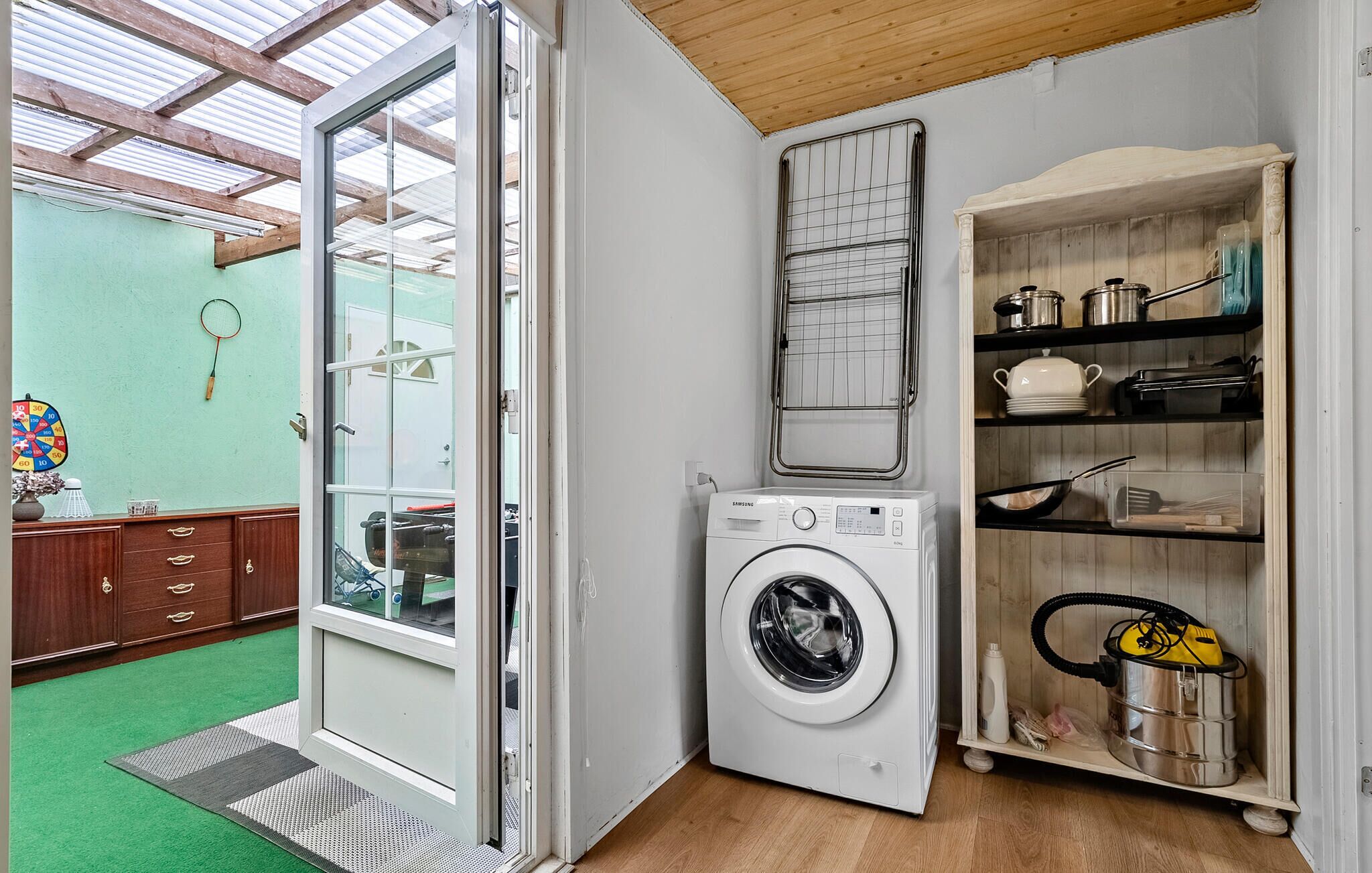 A compact laundry room with a washing machine, drying rack, and shelves with kitchenware.