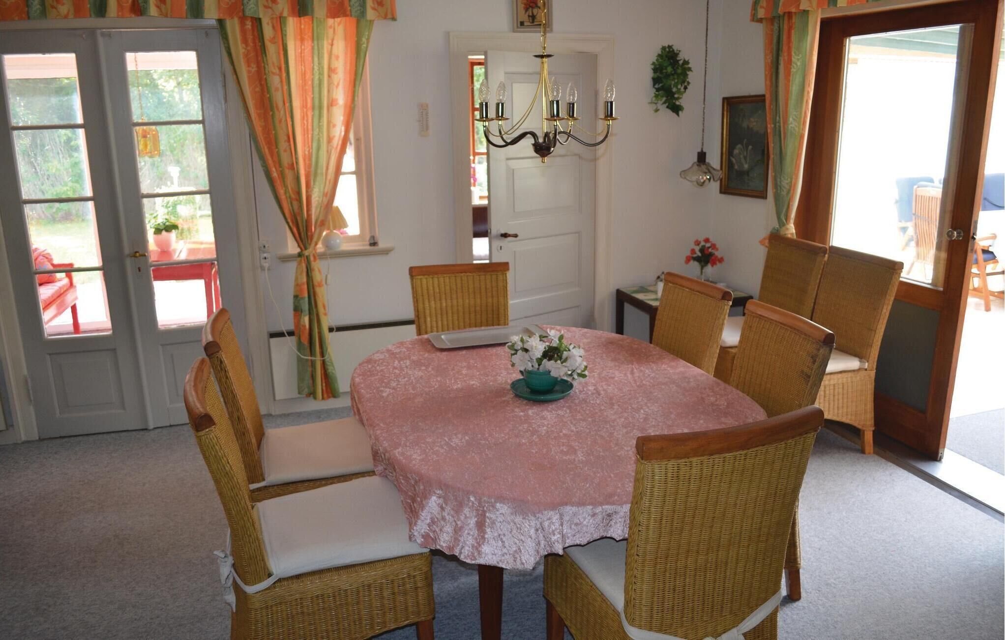 Un comedor con una mesa redonda, sillas de mimbre y un mantel rosa.