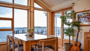 A dining area with a table and chairs, a guitar, a potted plant, and a view of the water. - Nice home in Nedstrand with sauna (Nedstrand)