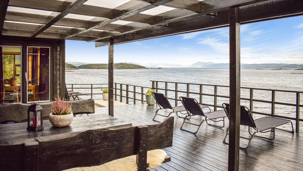 A covered outdoor deck with a wooden table and chairs, overlooking a body of water with distant landforms. - Nice home in Nedstrand with sauna (Nedstrand)