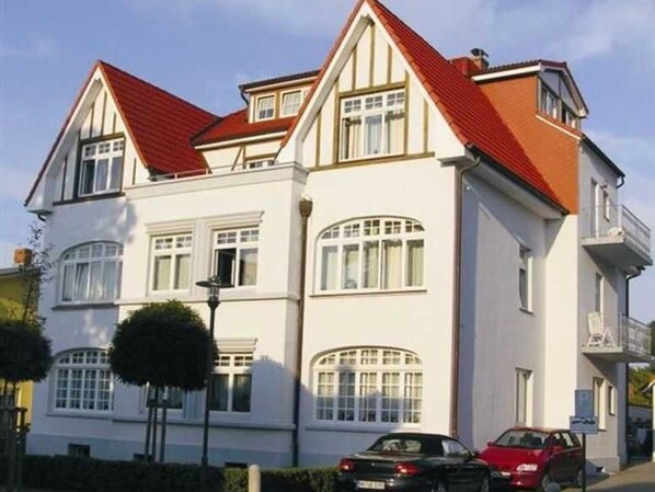 Un bâtiment à deux étages, avec un toit rouge et des murs blancs, doté de nombreuses fenêtres et d’un petit arbre devant.