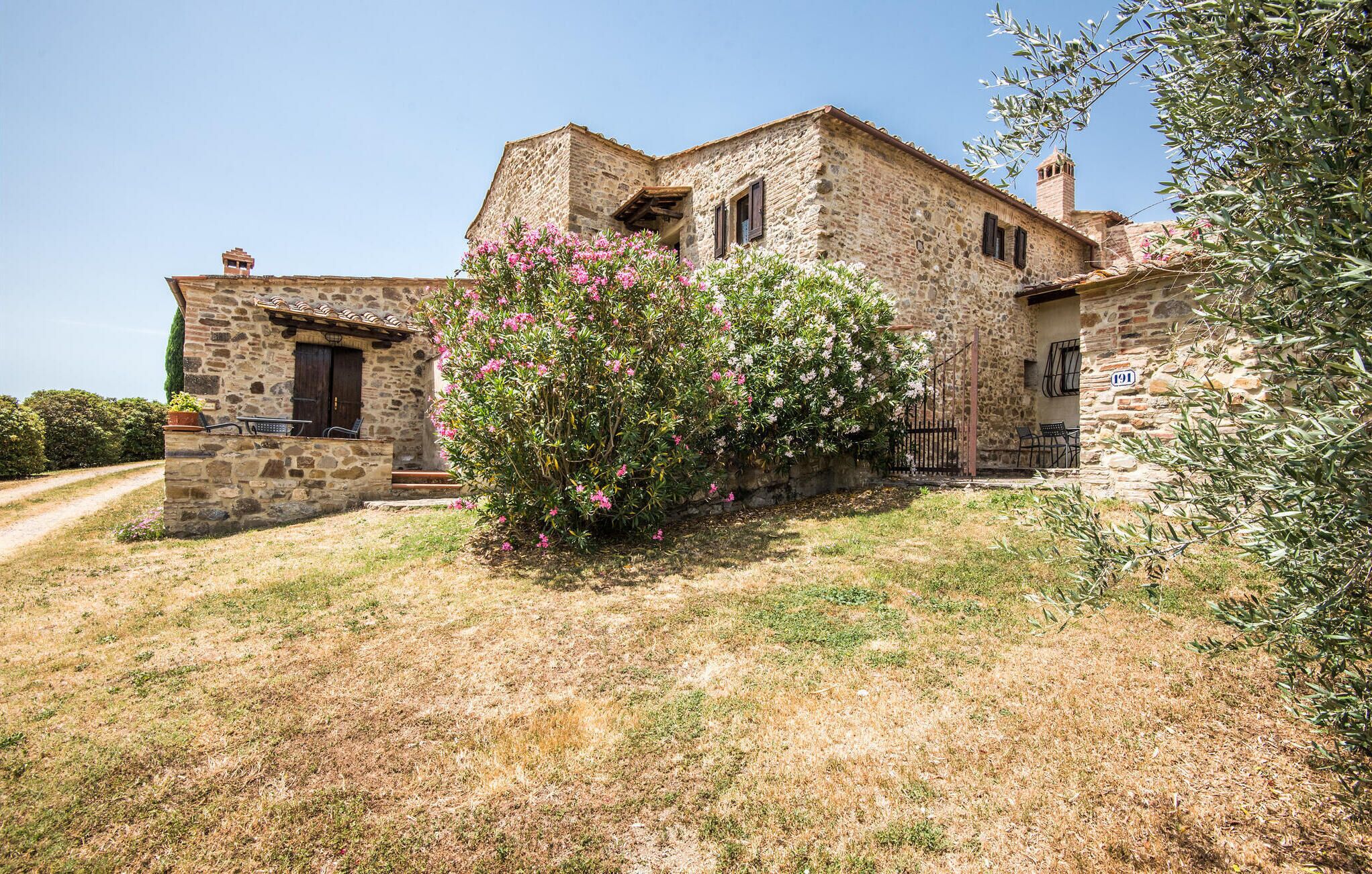 Un bâtiment en pierre à l’aspect rustique, doté d’un petit porche et d’un jardin agrémenté de fleurs roses.