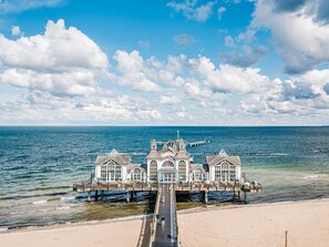 Un hotel frente al mar con un muelle que se adentra en el océano, con varios edificios de grandes ventanales y una torre central.