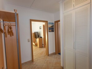 A hallway with a wooden wardrobe, a coat rack, and a door leading to a room with a desk and a television.