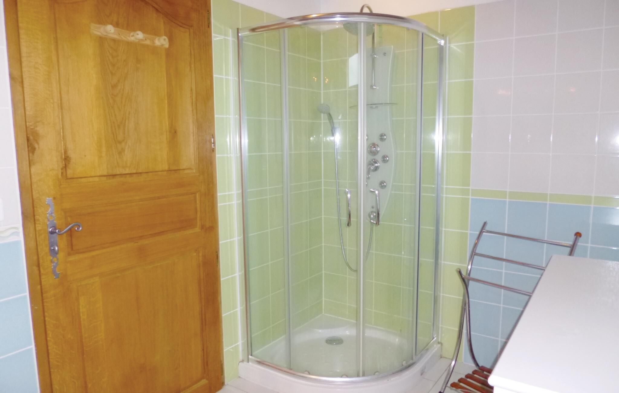 Un box de ducha con puerta de vidrio, una puerta de madera a la izquierda y paredes de azulejos.