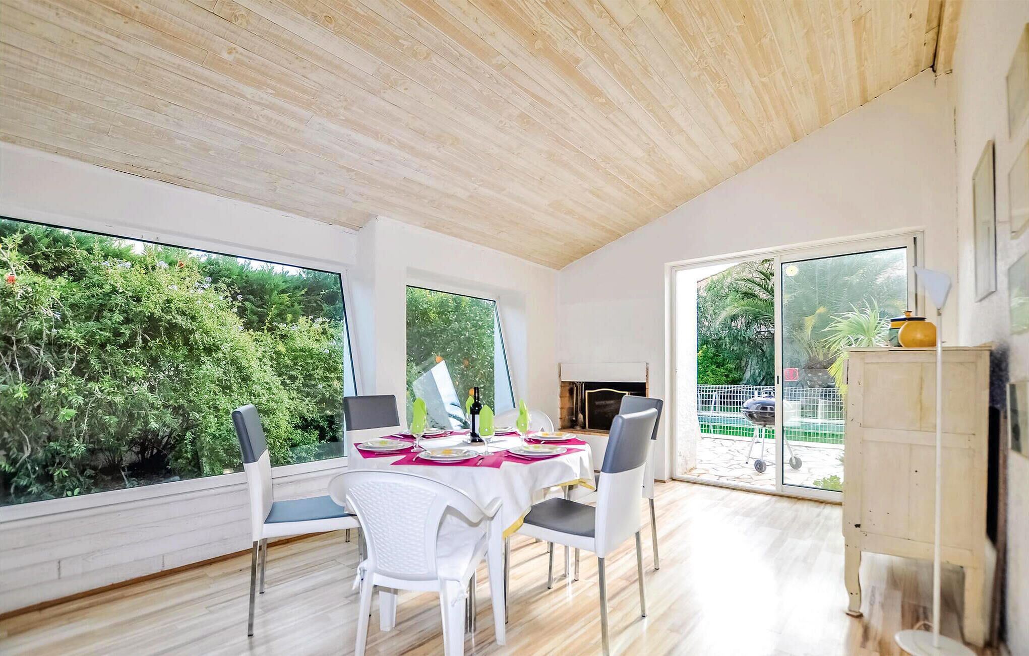 A dining area with a table set for four, large windows, and a view of greenery outside.