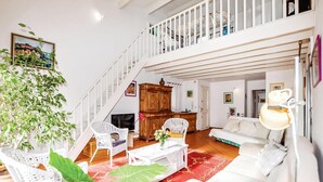 Amplia sala de estar con una escalera, mobiliario blanco y una planta grande.