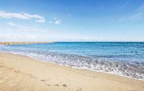 Ein Strand mit klarem, blauem Wasser, einem Sandstrand und einem Felsenmole im Hintergrund.