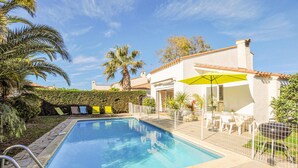 Una piscina con patio amurallado, sillas de descanso y zona de estar cubierta al aire libre.